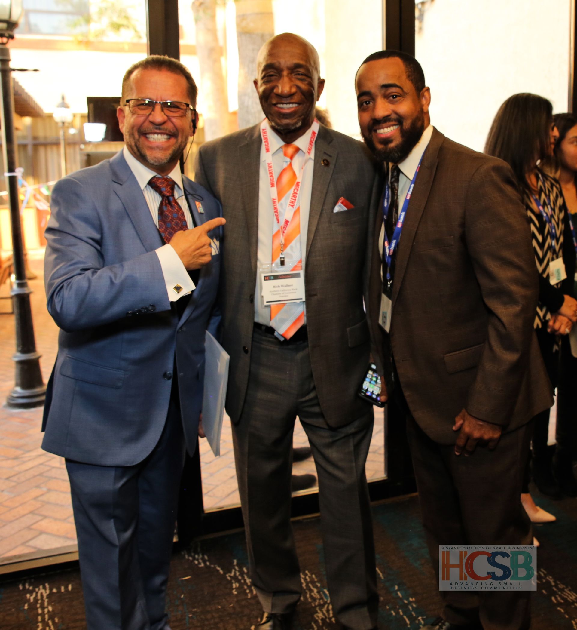 Three men in suits and ties pose for a photo in front of a hcsb logo