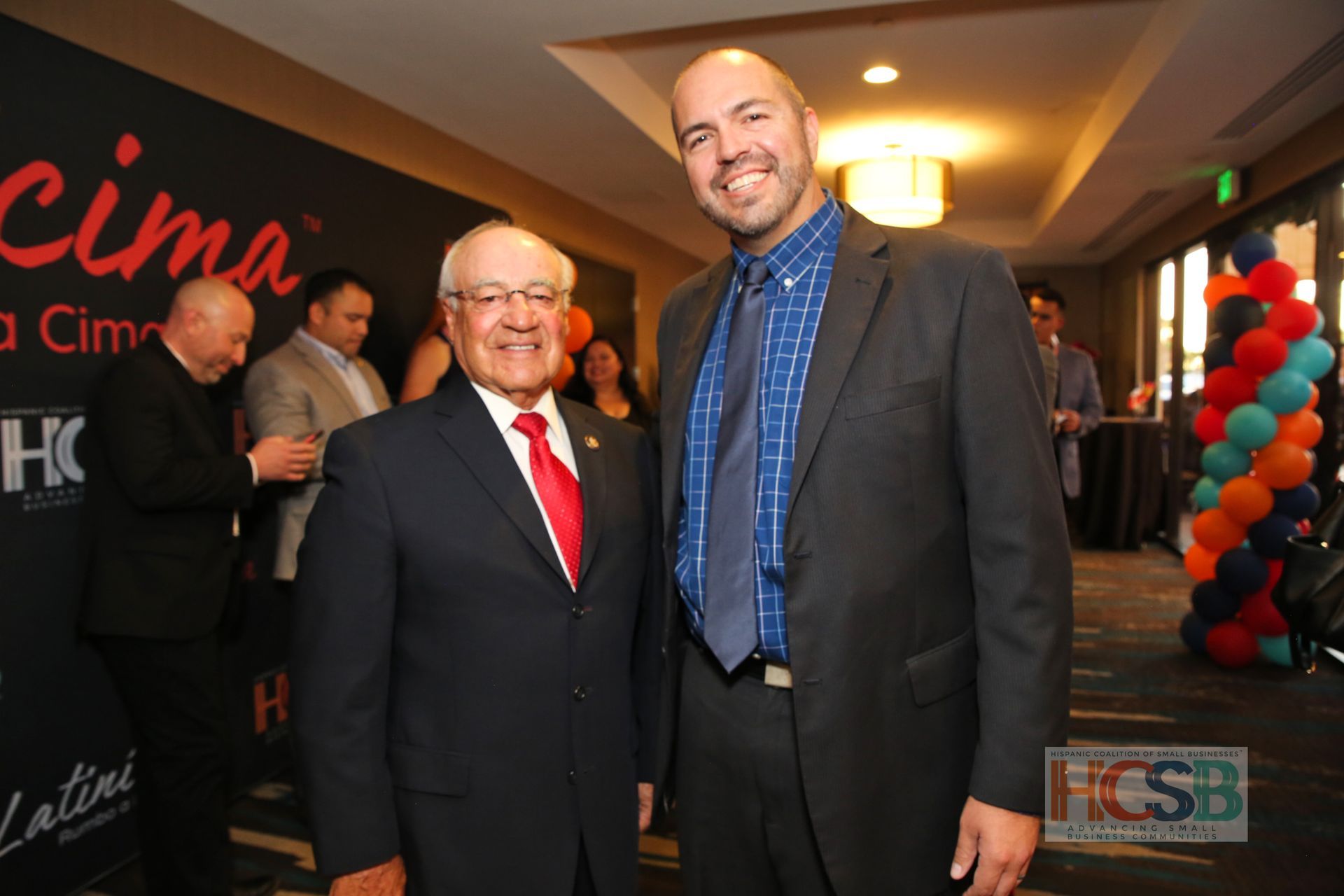 Two men are posing for a picture in front of a sign that says cima