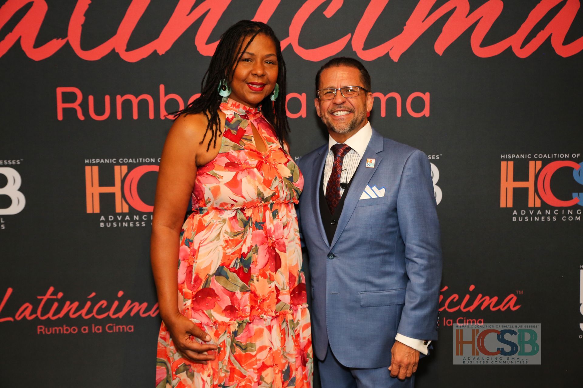 A man and a woman are posing for a picture in front of a sign that says hcsb