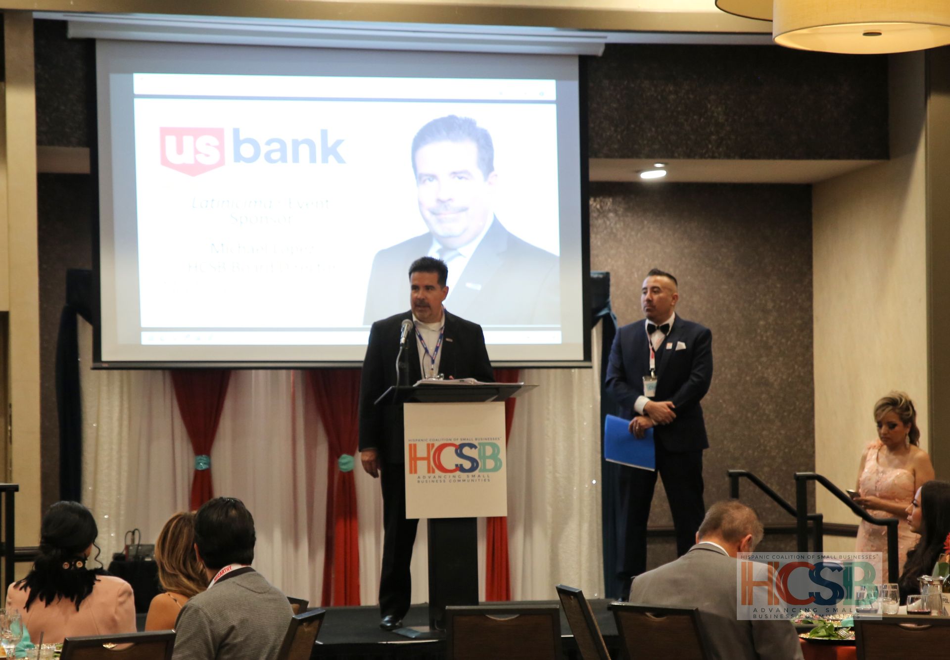 A man stands at a podium in front of a screen that says ub bank