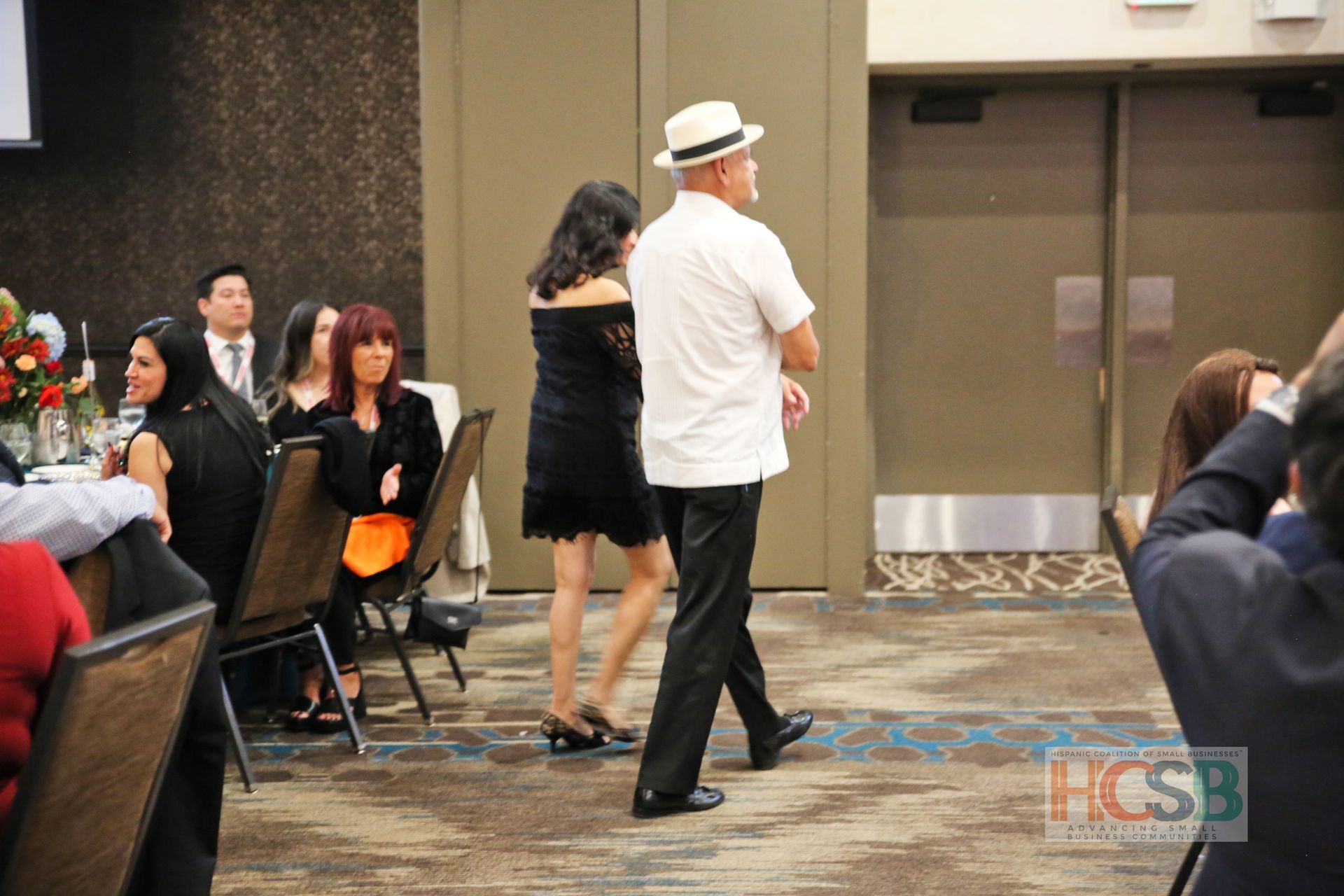 A man in a white hat is dancing with a woman in a black dress.