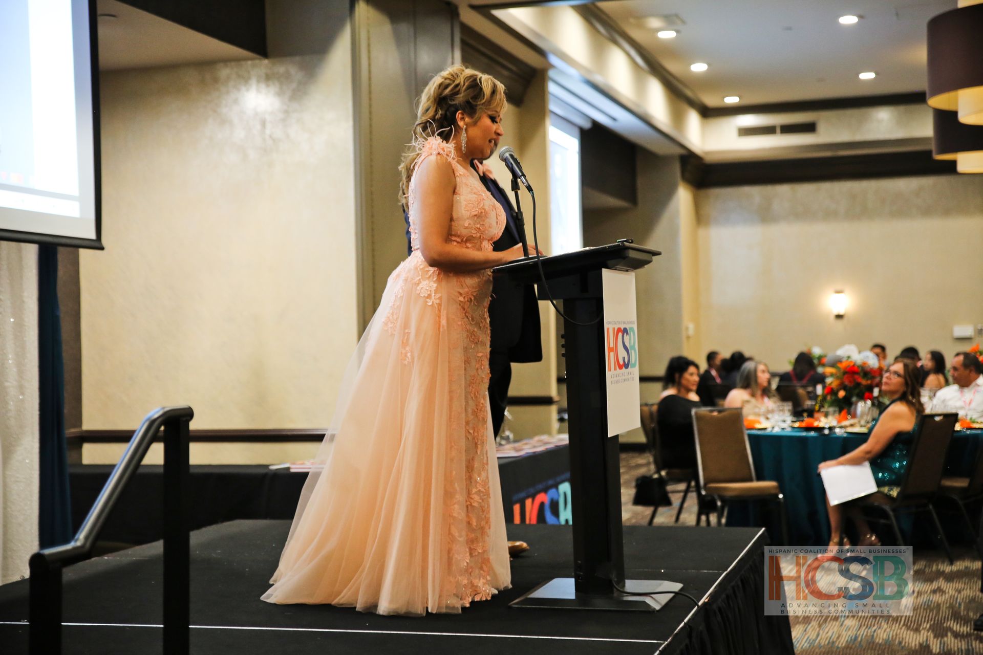 A woman in a pink dress is standing at a podium giving a speech.