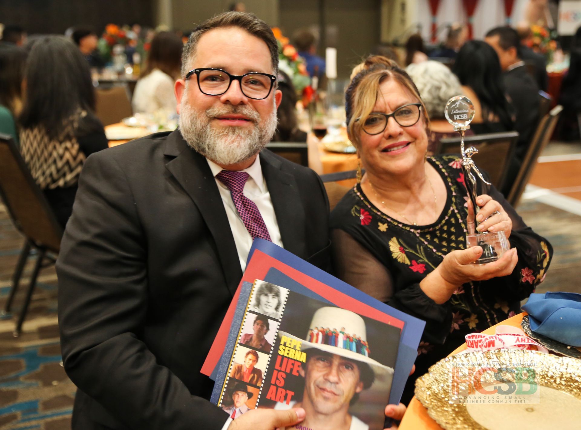 A man and a woman are holding a book and a trophy.
