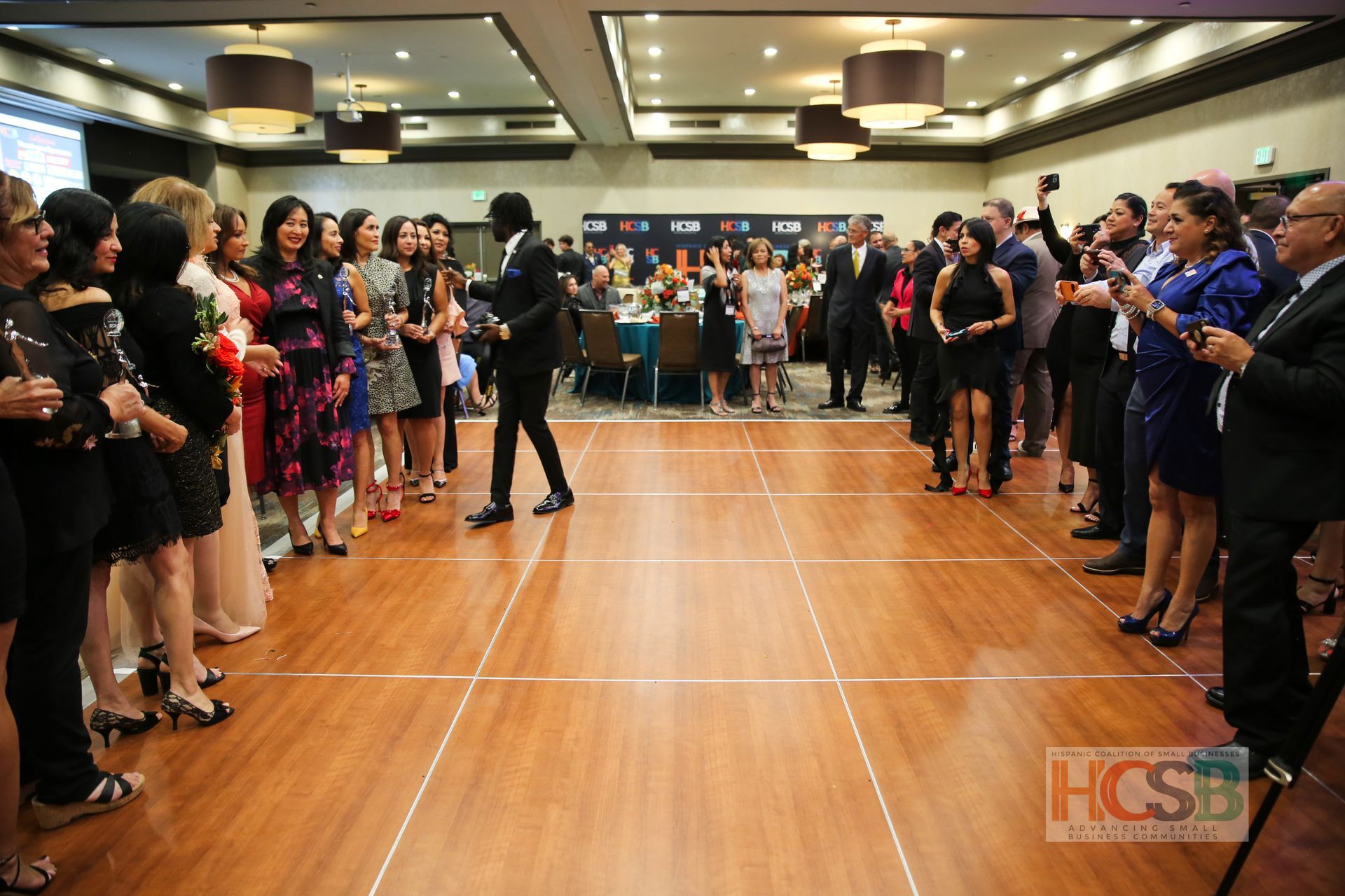 A group of people are standing around a dance floor with the word hcsb on the bottom