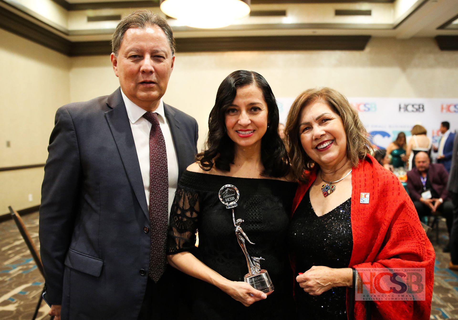 A man in a suit and tie is standing next to two women holding a trophy.