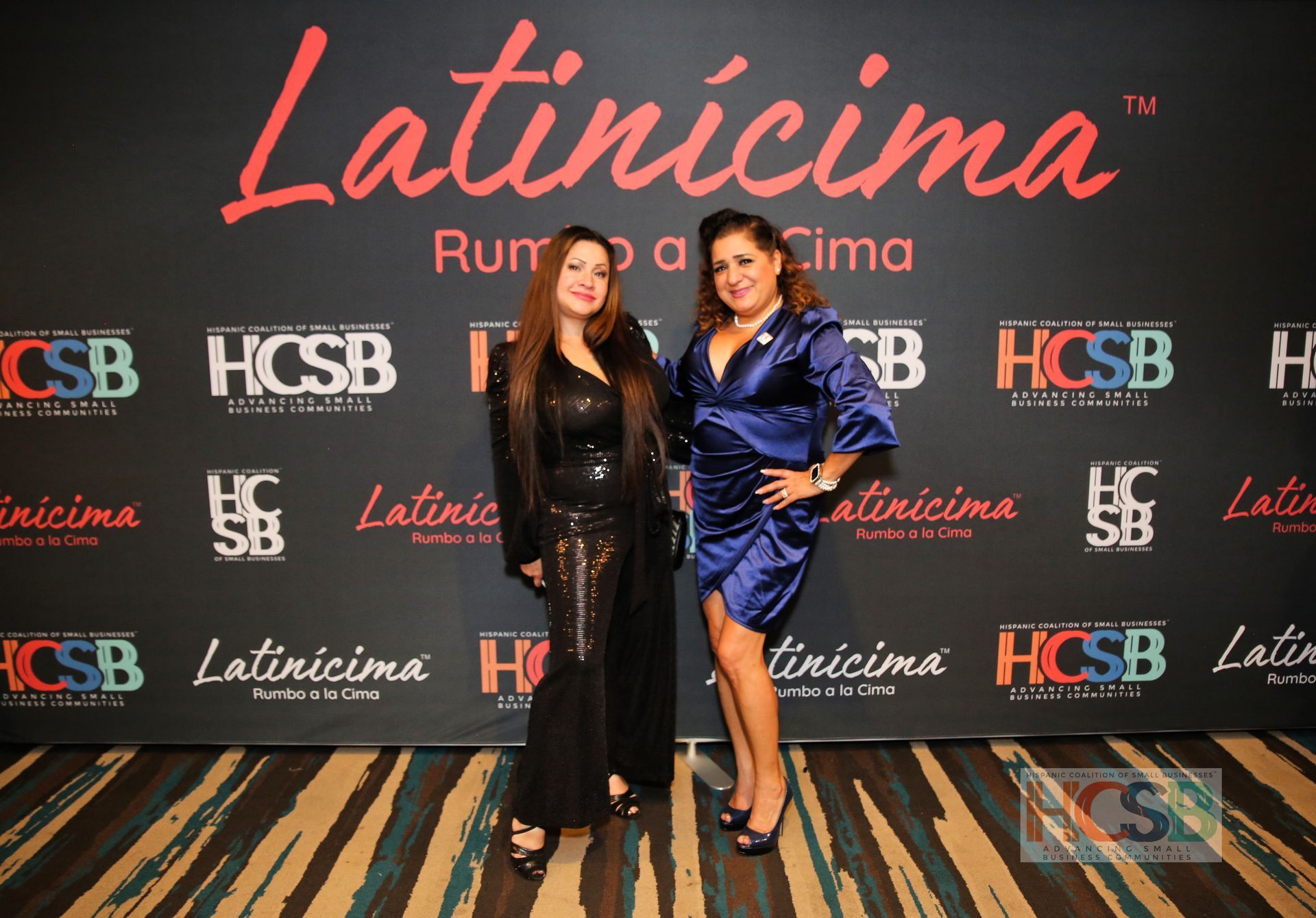 Two women standing in front of a wall that says latincima