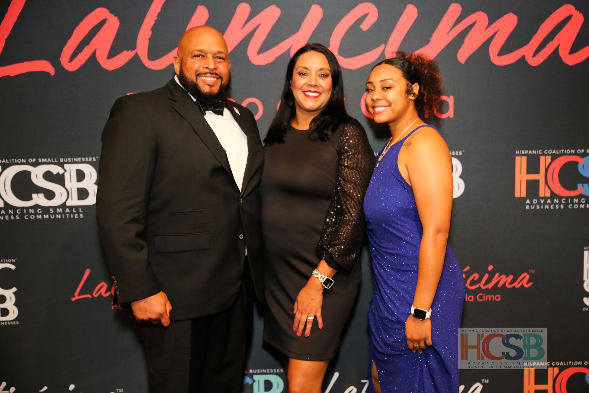 Three people posing for a picture in front of a wall that says csb