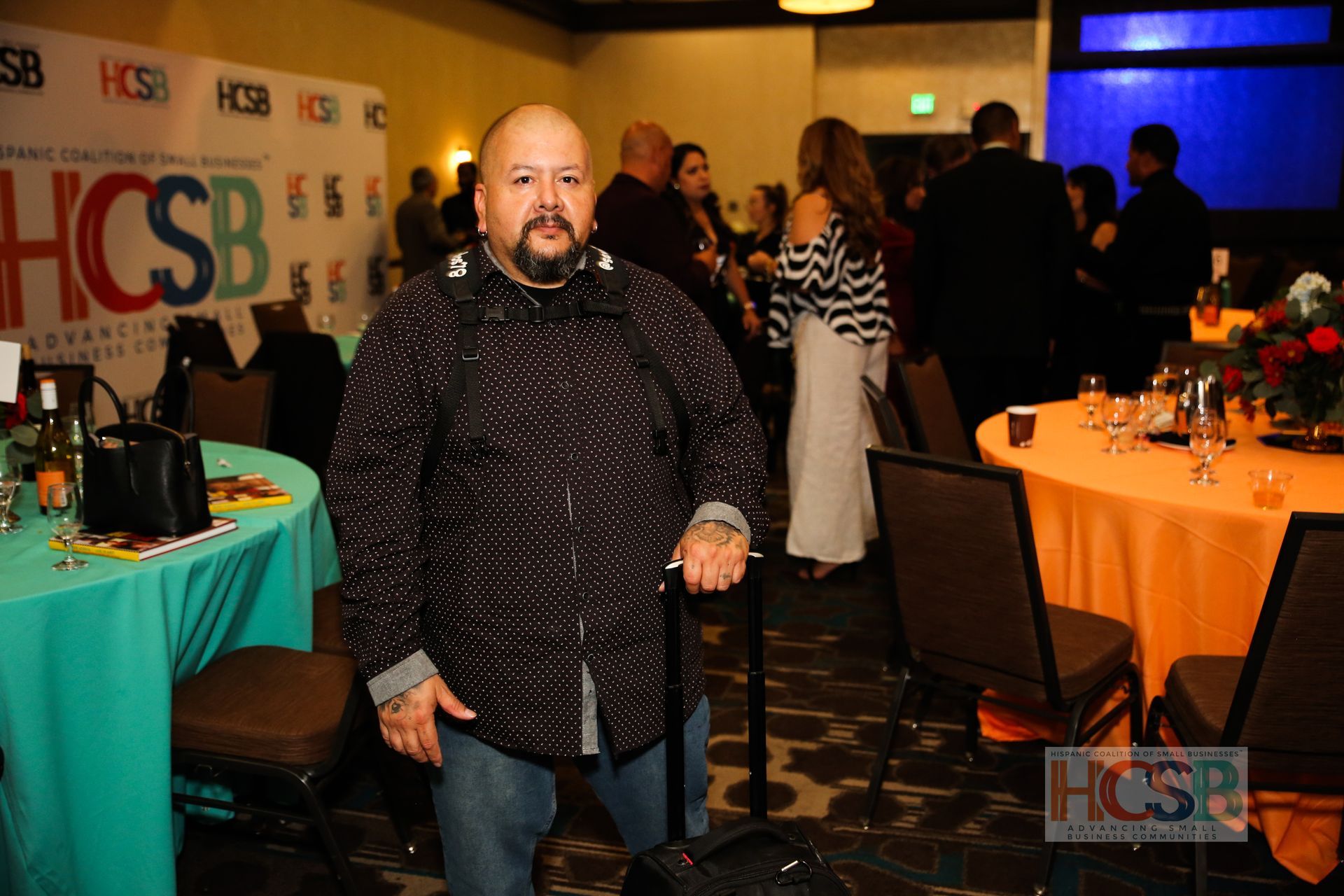 A man is standing in a room with tables and chairs and a sign that says hcsb