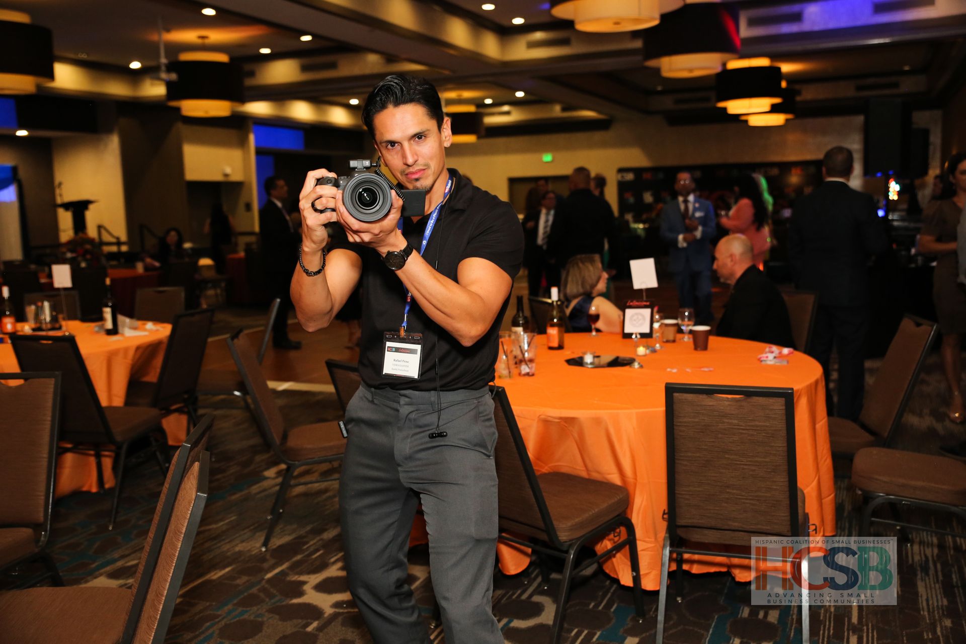 A man taking a picture with a camera in a room with tables and chairs