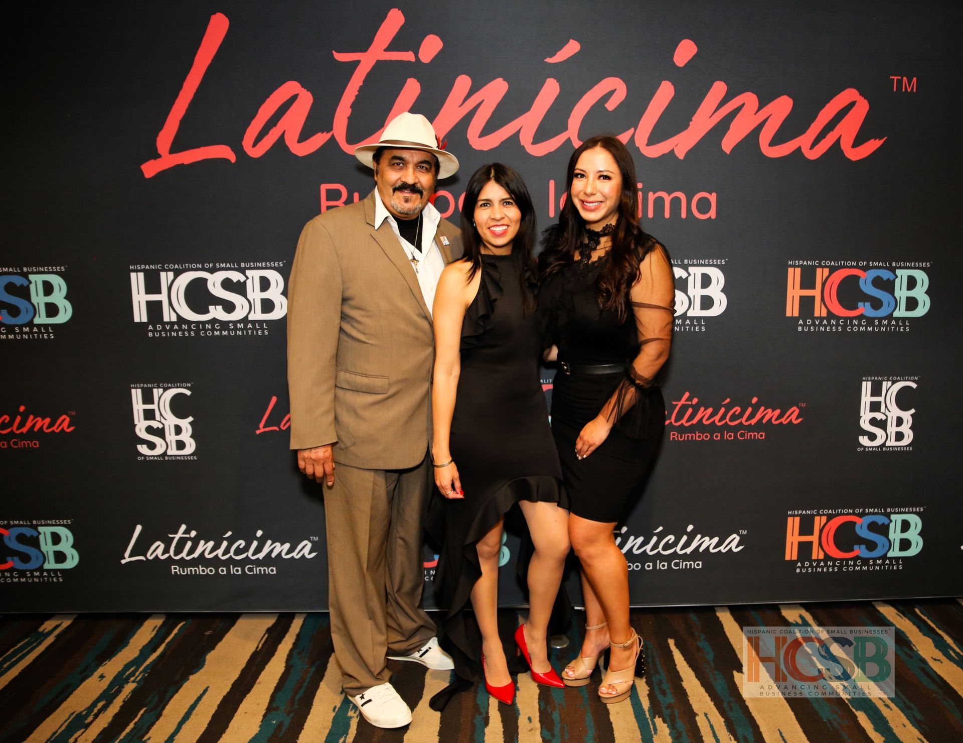 Three people are posing for a picture in front of a wall that says latincima