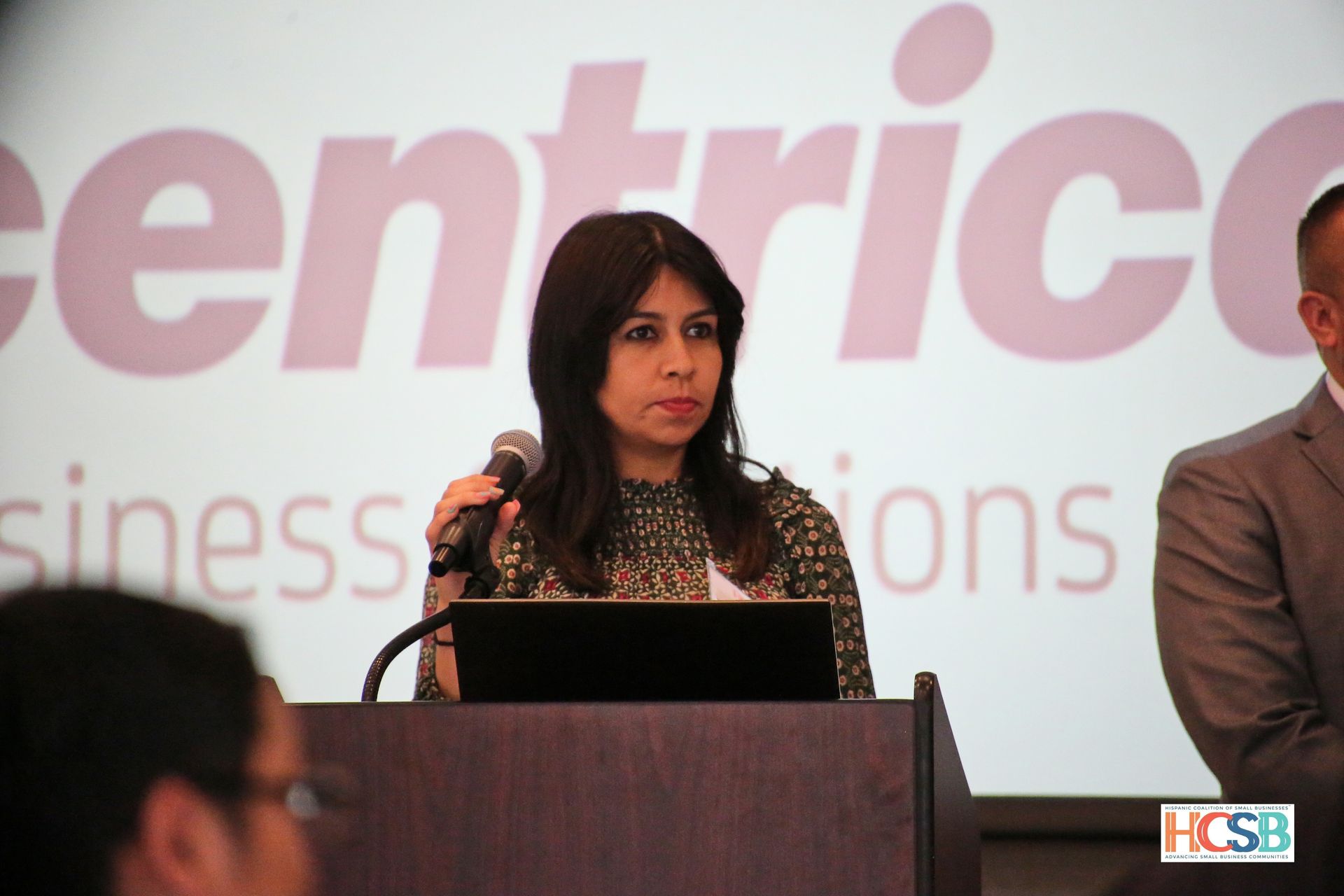 A woman stands at a podium in front of a screen that says centric business solutions