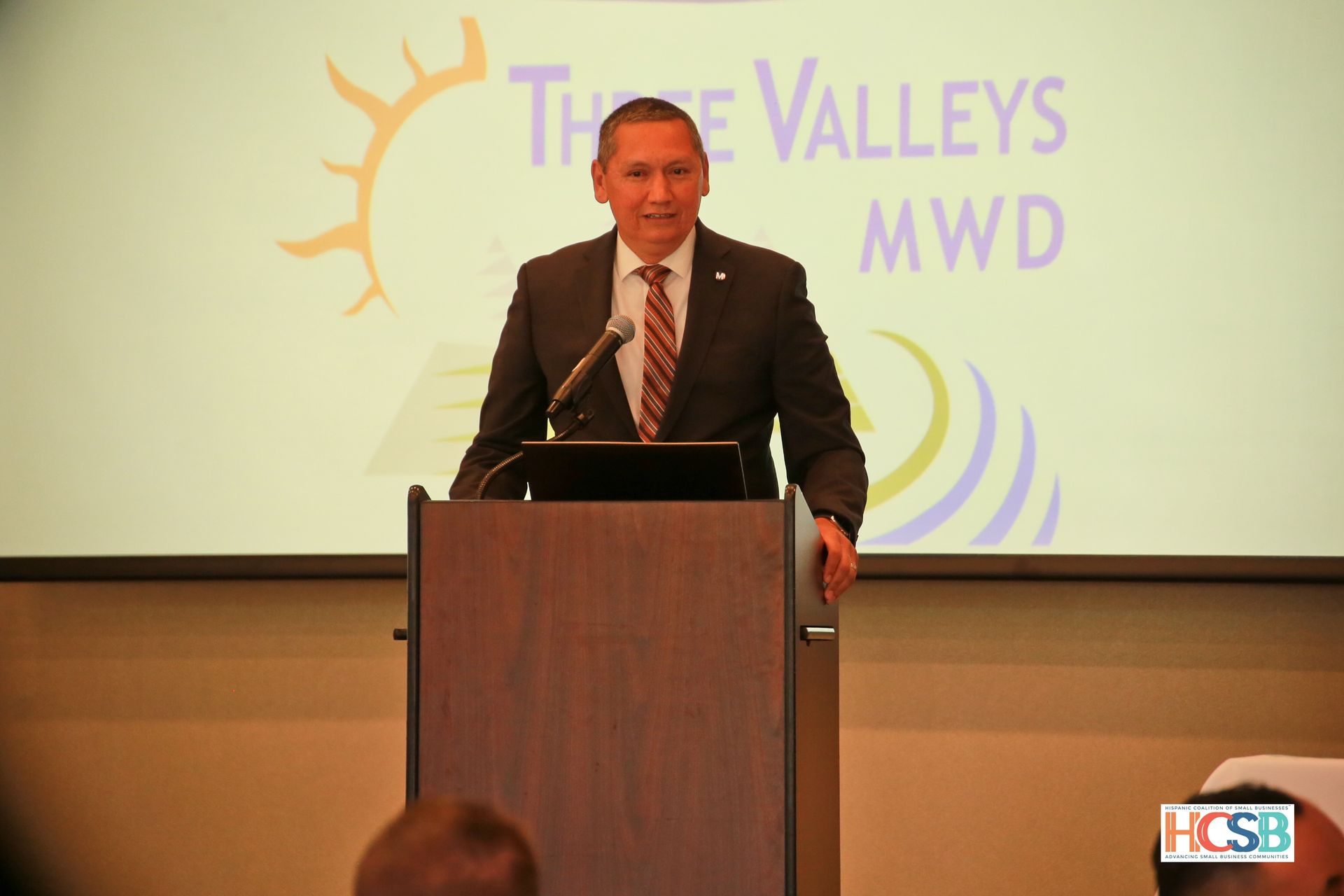 A man stands at a podium in front of a screen that says three valleys mwd