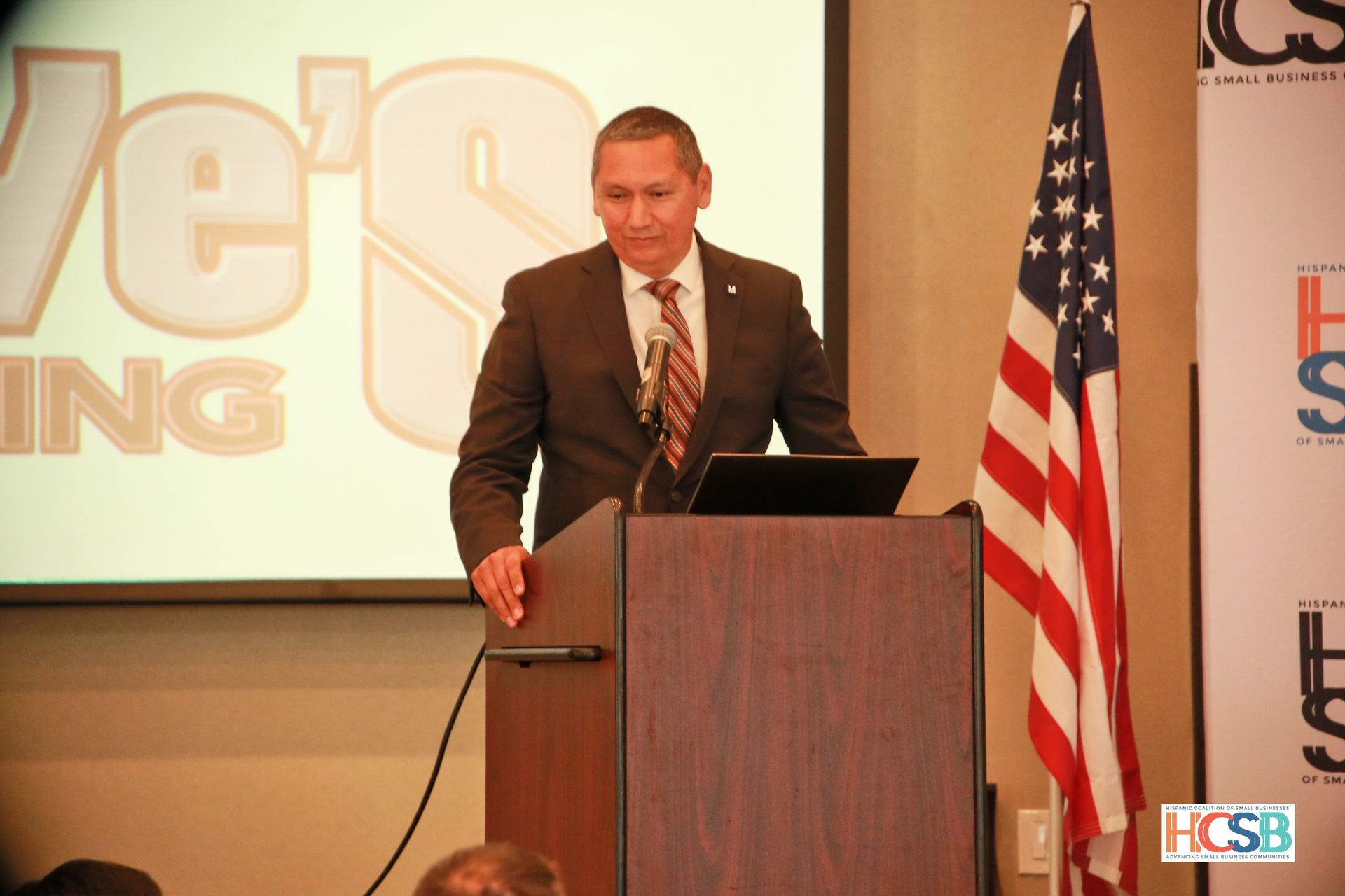 A man stands at a podium in front of a screen that says vet 's ing