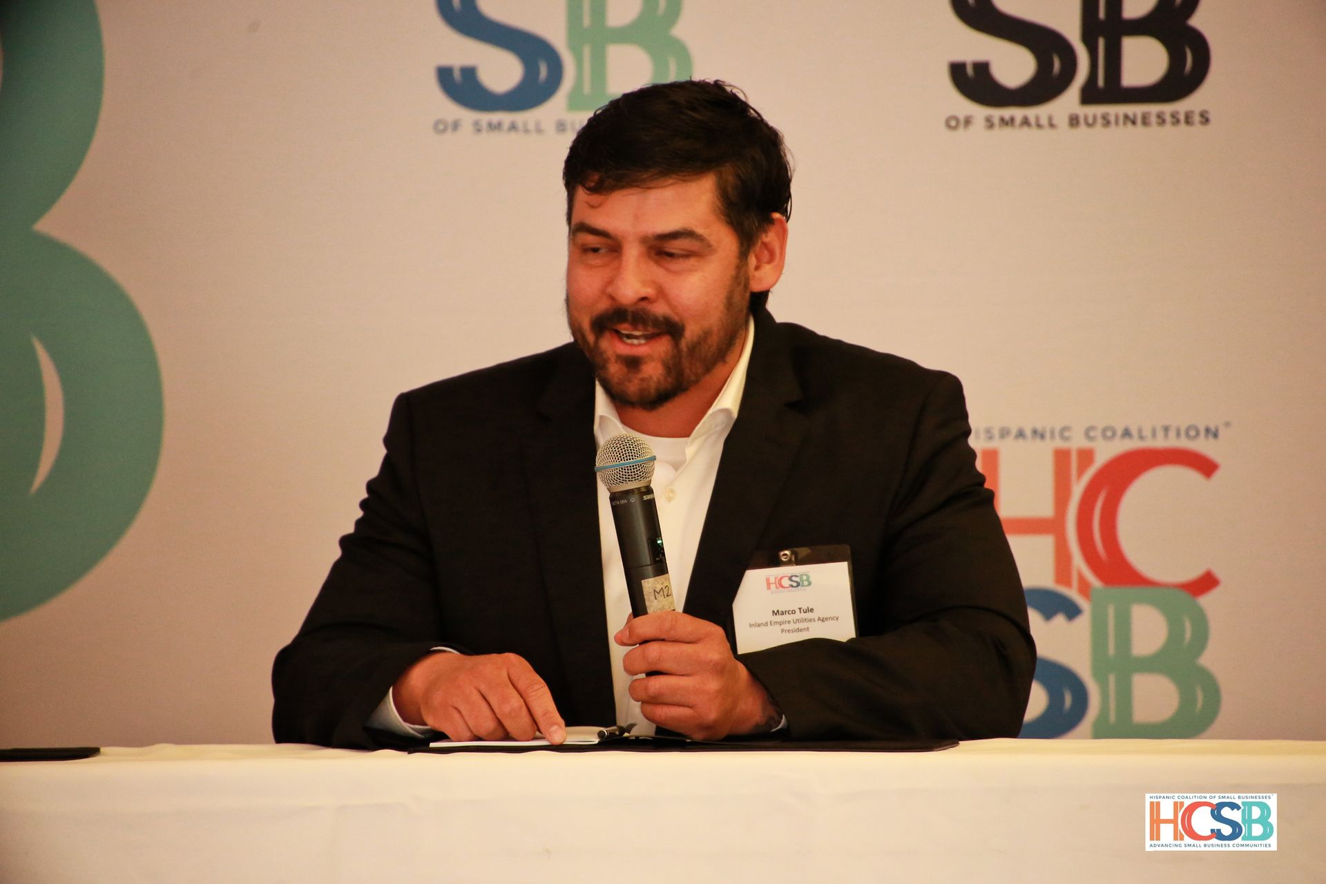 A man in a suit is sitting at a table holding a microphone