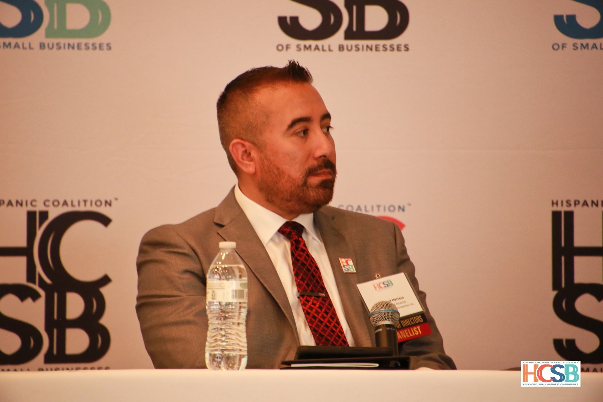 A man in a suit and tie is sitting at a table with a bottle of water.