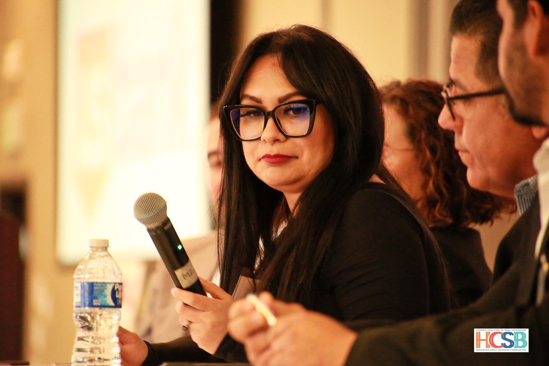 A woman is holding a microphone while sitting at a table with other people.