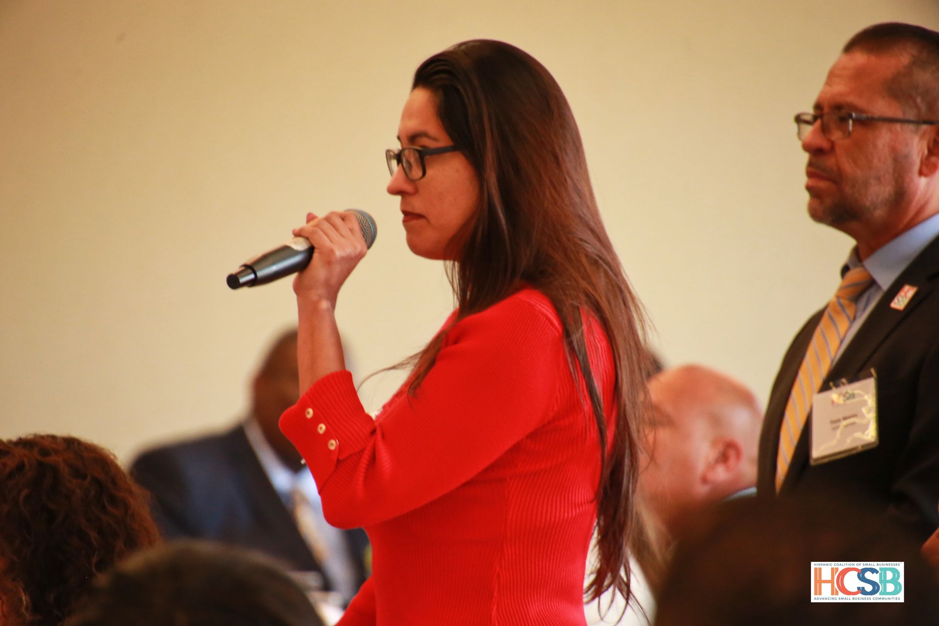A woman in a red jacket is speaking into a microphone.