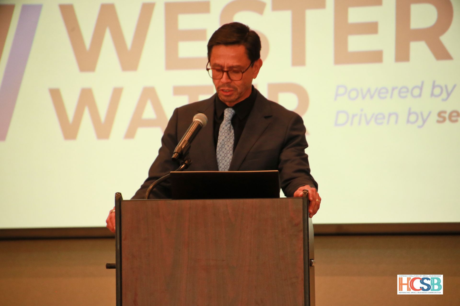 A man stands at a podium in front of a screen that says ' powered by driven by se '