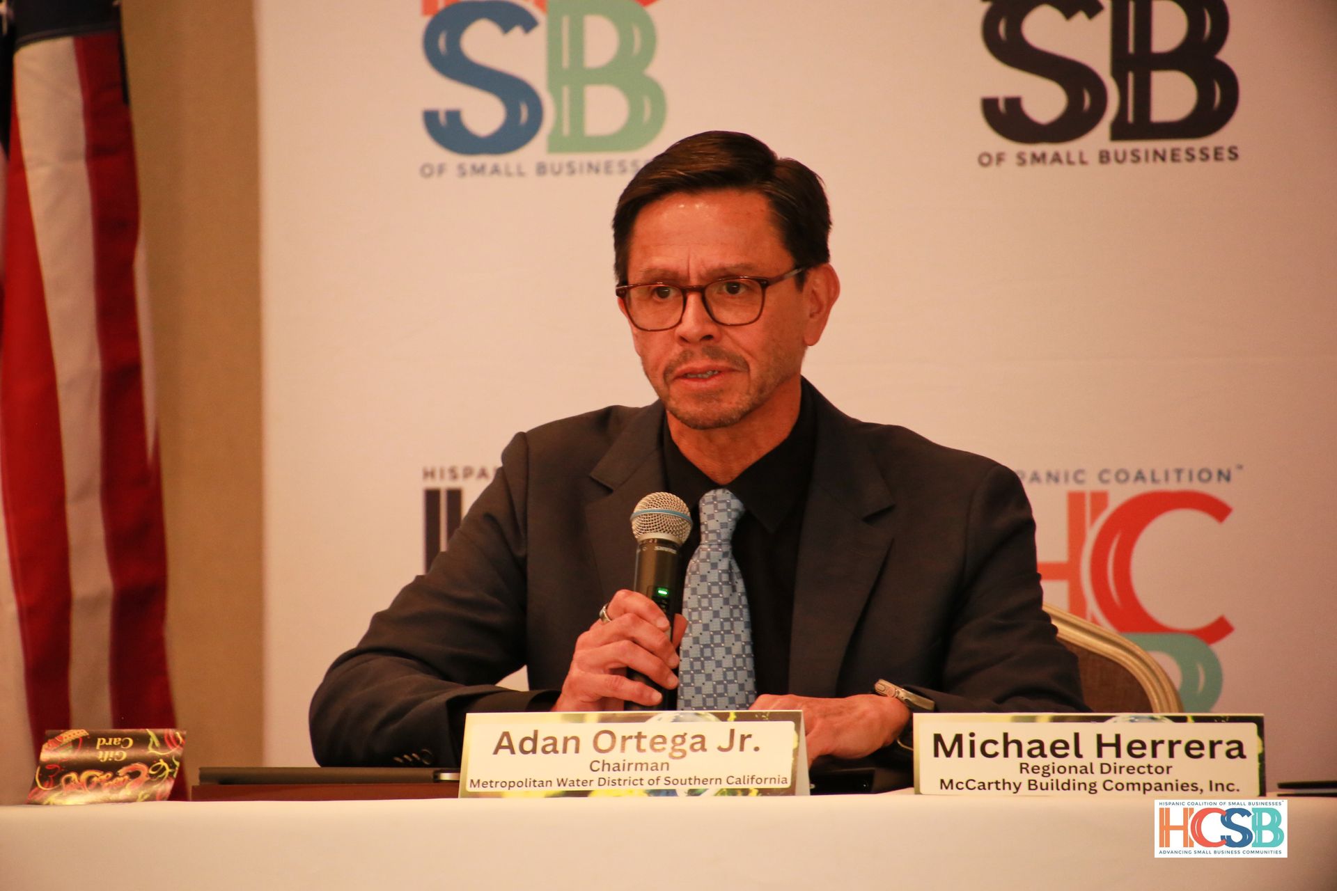 A man in a suit and tie is sitting at a table with a microphone.