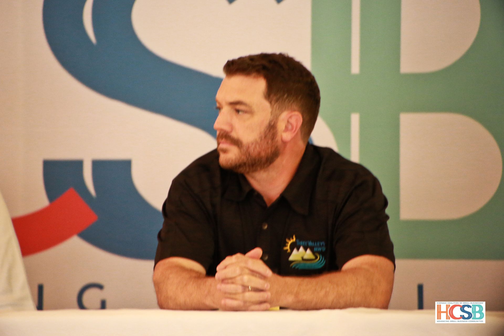 A man sits at a table in front of a hcsb logo