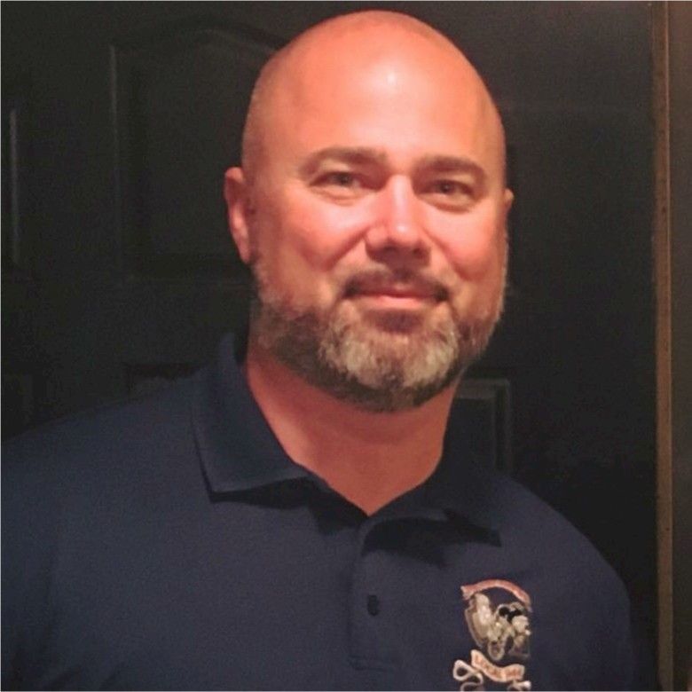 A bald man with a beard is wearing a blue polo shirt