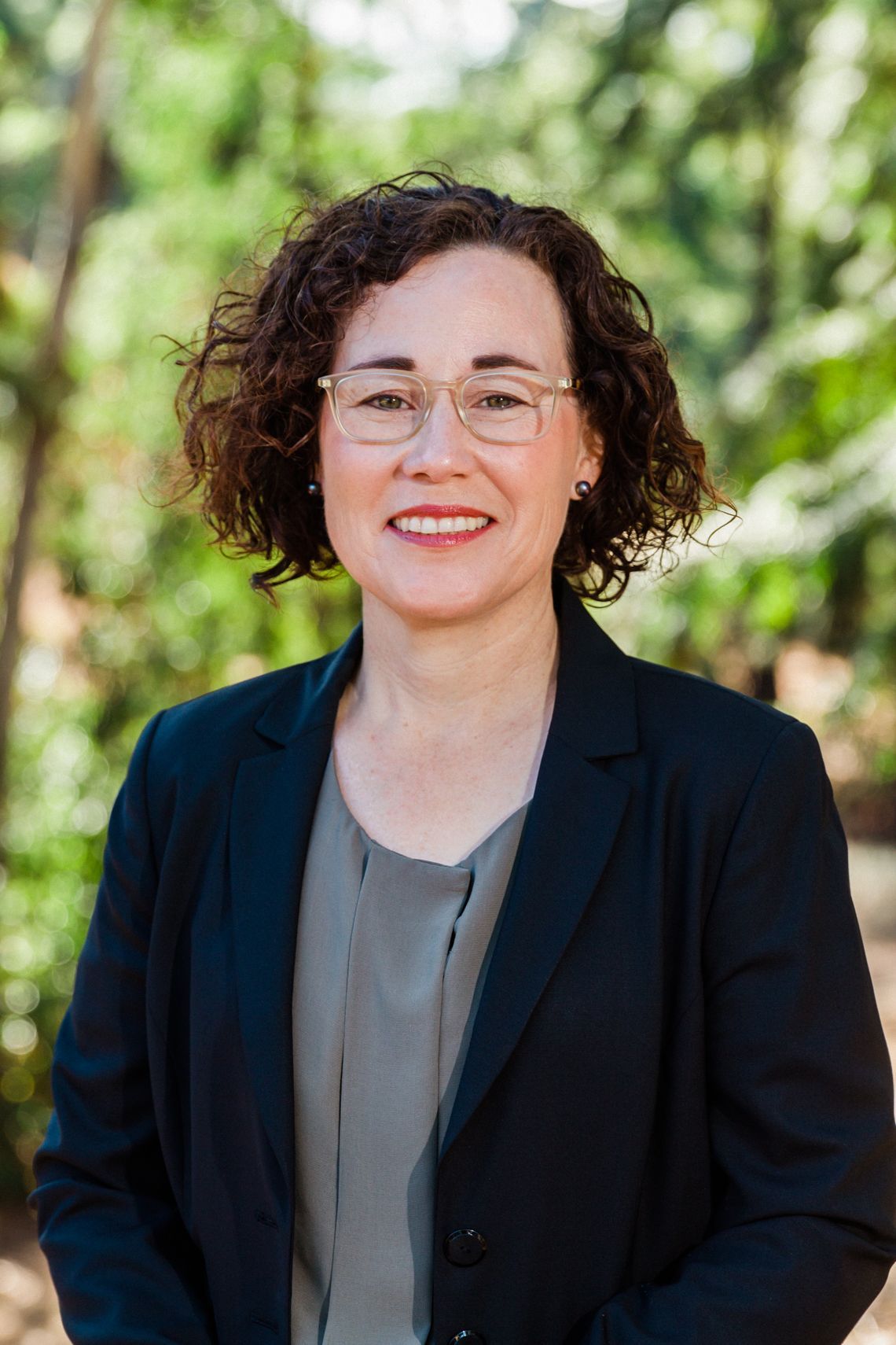 A woman wearing glasses and a black jacket is smiling for the camera.
