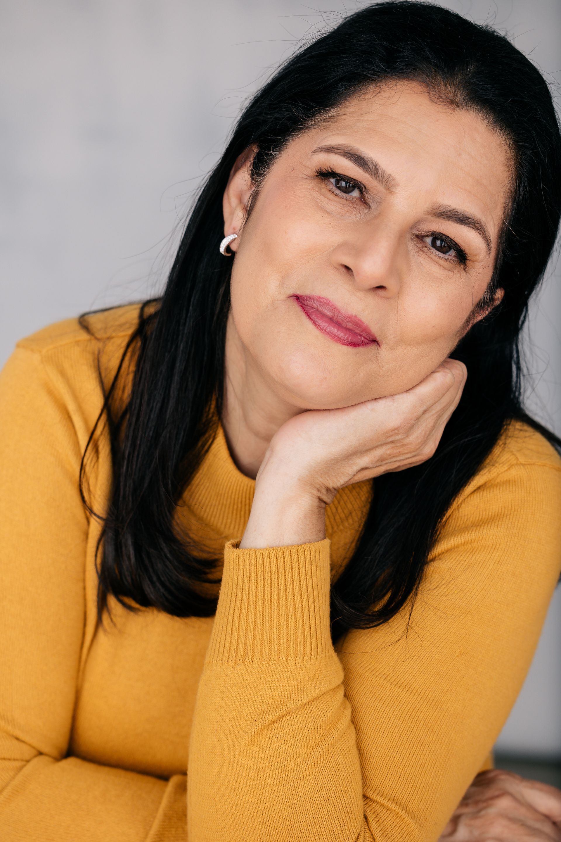 The woman is wearing a yellow sweater and has her hand on her chin.