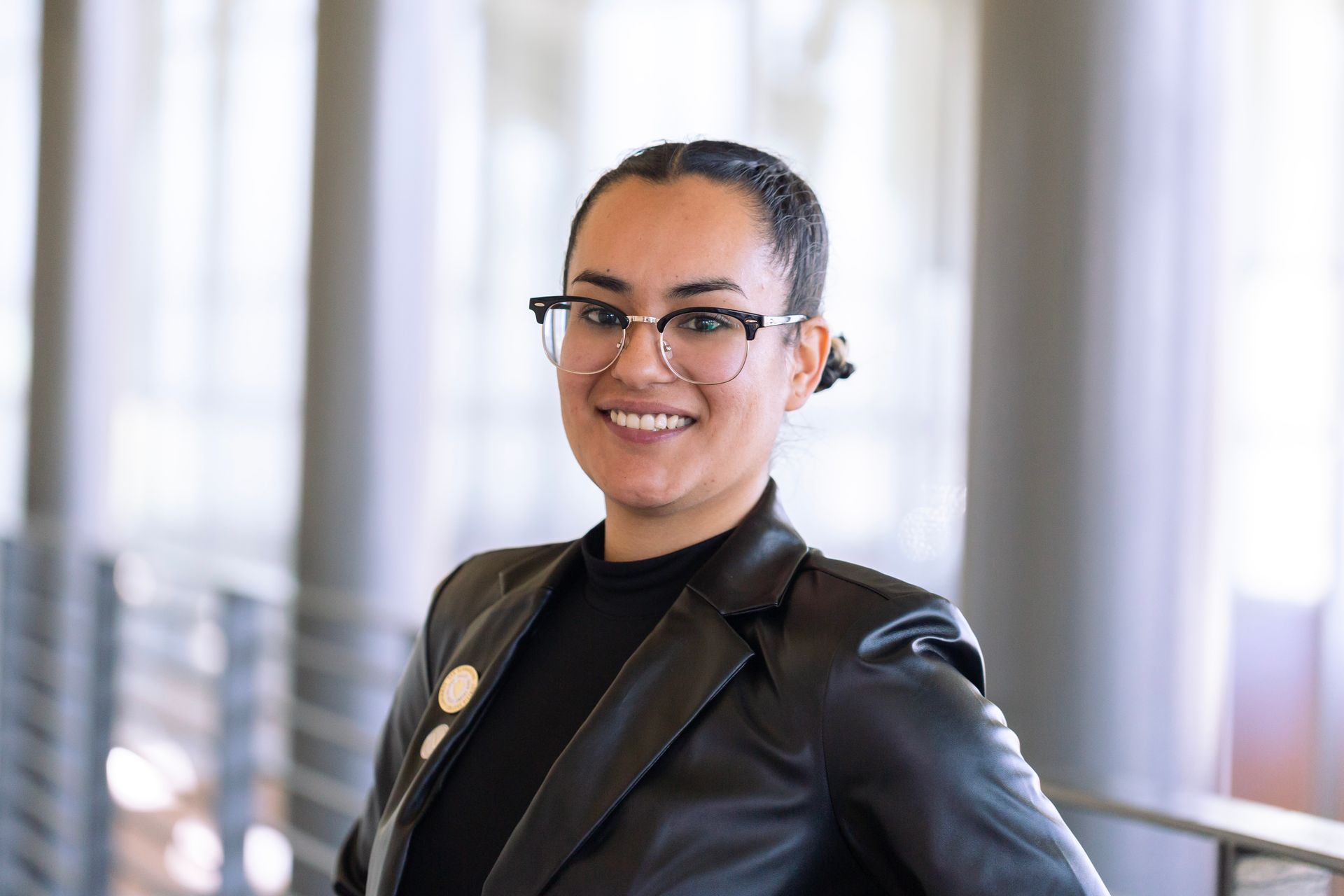 A woman wearing glasses and a black leather jacket is smiling for the camera.
