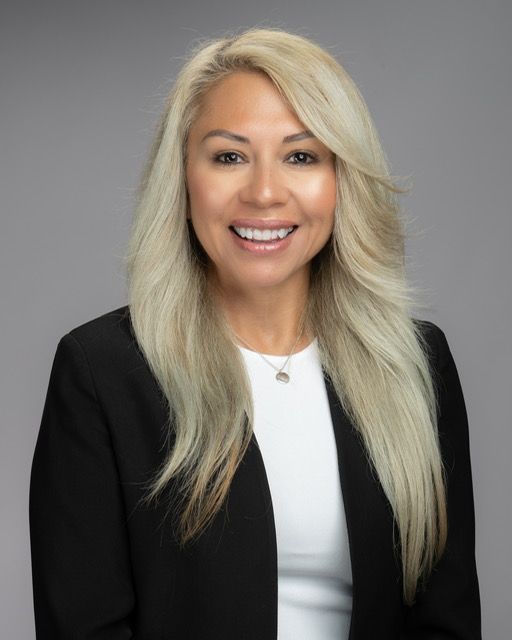 A woman with long blonde hair is wearing a black jacket and a white shirt.