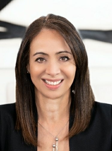 A woman wearing a black jacket and a necklace is smiling for the camera.