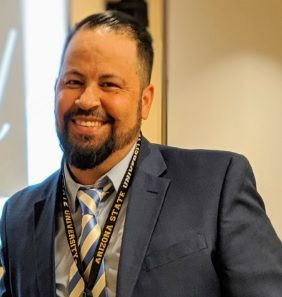 A man in a suit and plaid shirt is smiling for the camera.