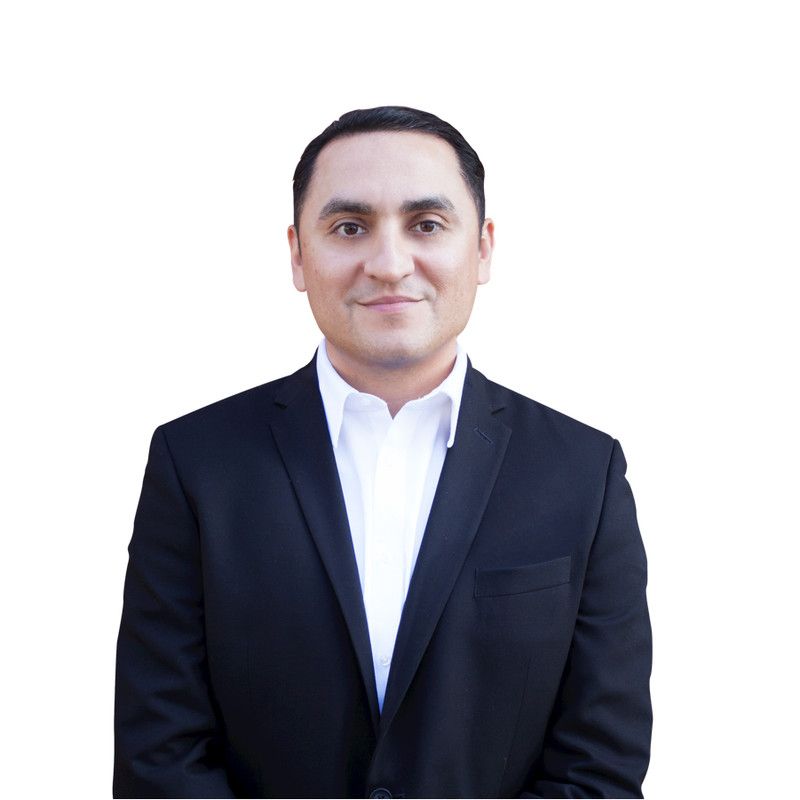 A man in a suit and white shirt stands in front of a white background