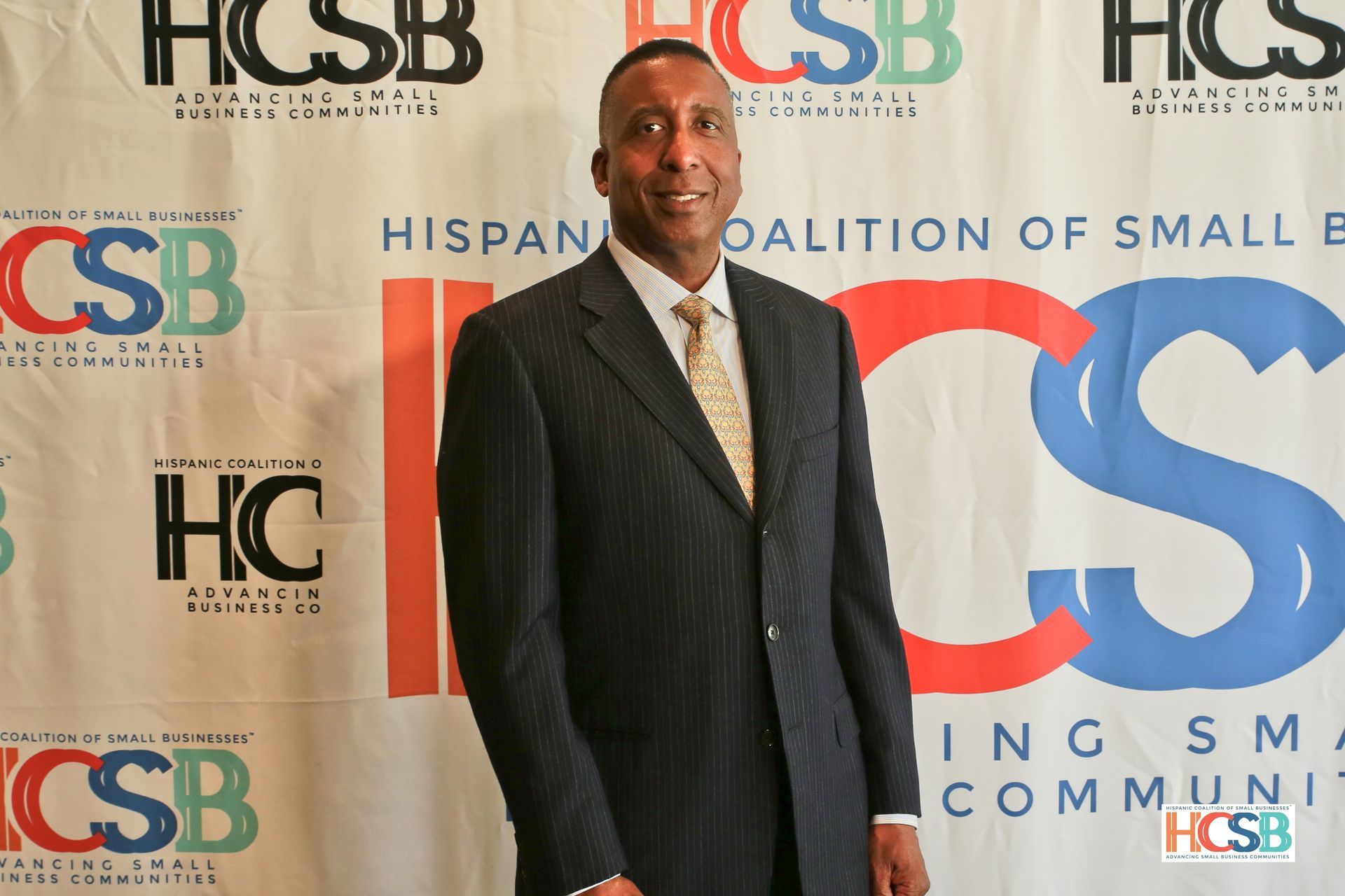 A man in a suit and tie stands in front of a hcsb banner