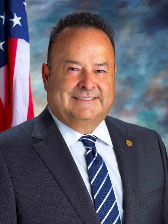 A man in a suit and tie is smiling in front of an american flag.