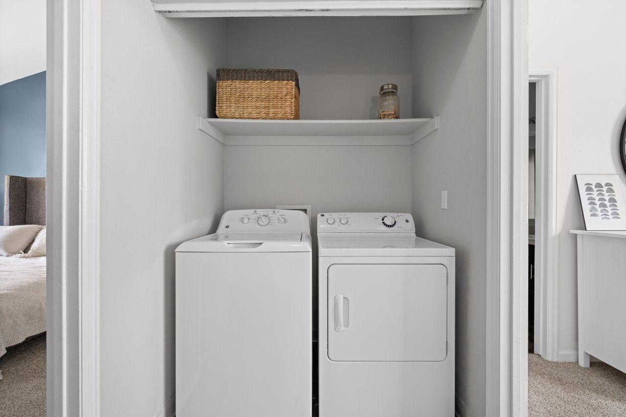Laundry closet with a washer and dryer side by side and a shelf above.