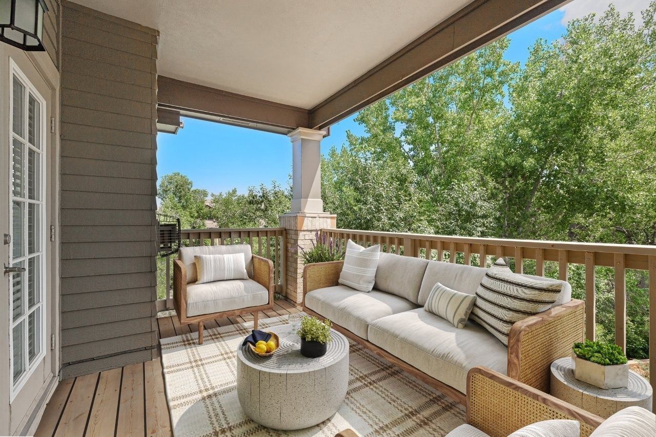 Outdoor apartment balcony with cream cushions, wicker seating, and a round coffee table.
