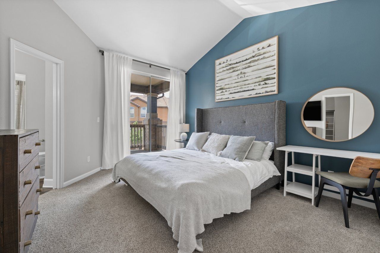 Bedroom in an apartment with a blue accent wall, upholstered bed, dresser, and balcony door.