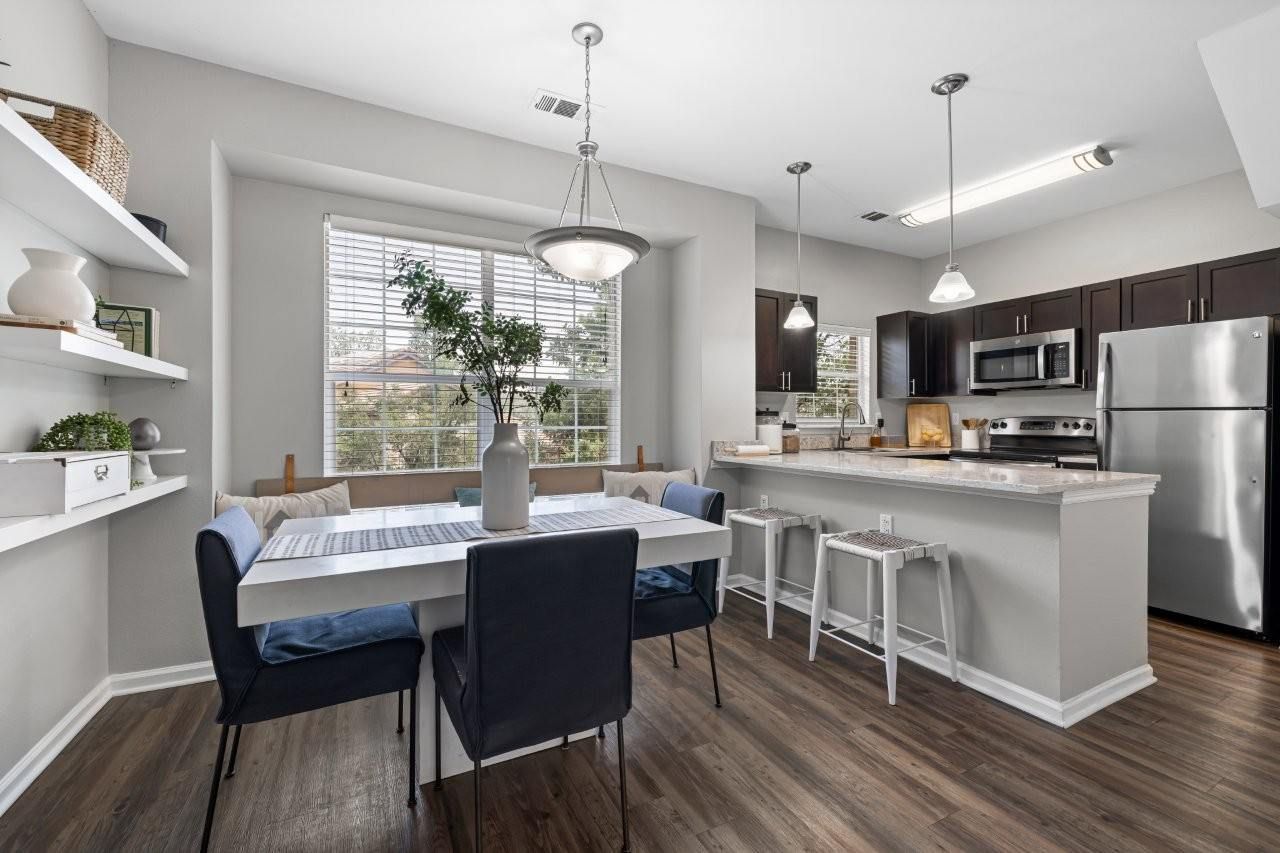 Open-plan dining area and kitchen in a modern apartment unit with a table and navy chairs.