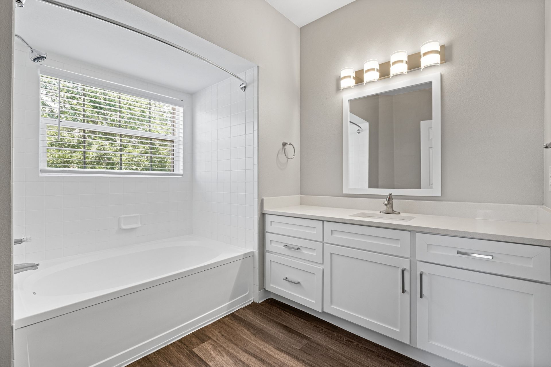 Bright bathroom with white tile shower, window with blinds, tub, and white single-sink vanity.