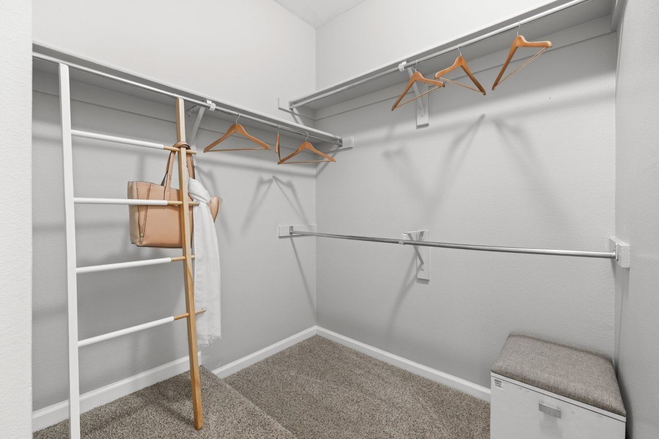 Walk-in closet with metal clothing rods, wooden hangers, and a cushioned bench.