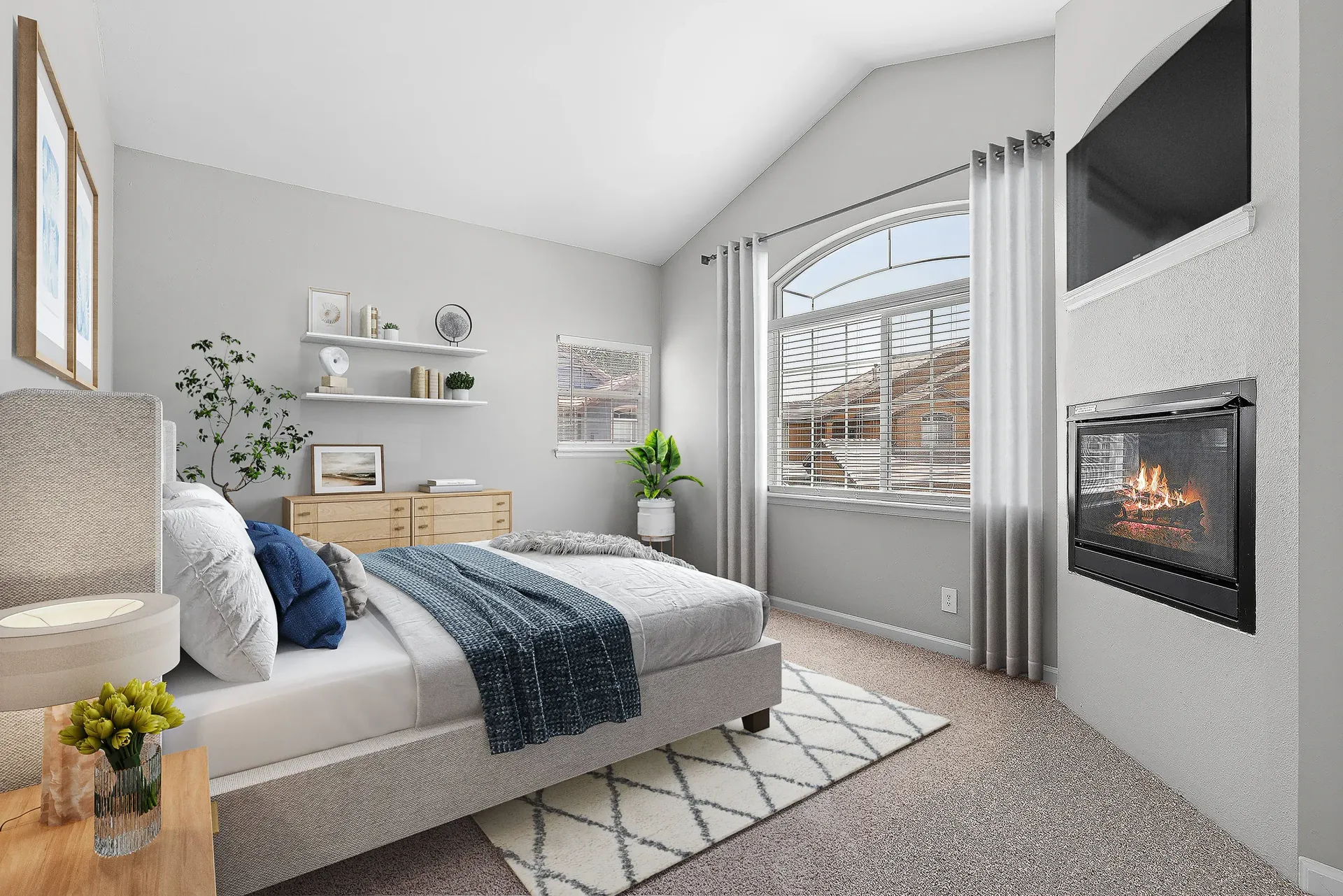 Neutral-toned apartment bedroom with a large arched window, fireplace, and mounted TV.