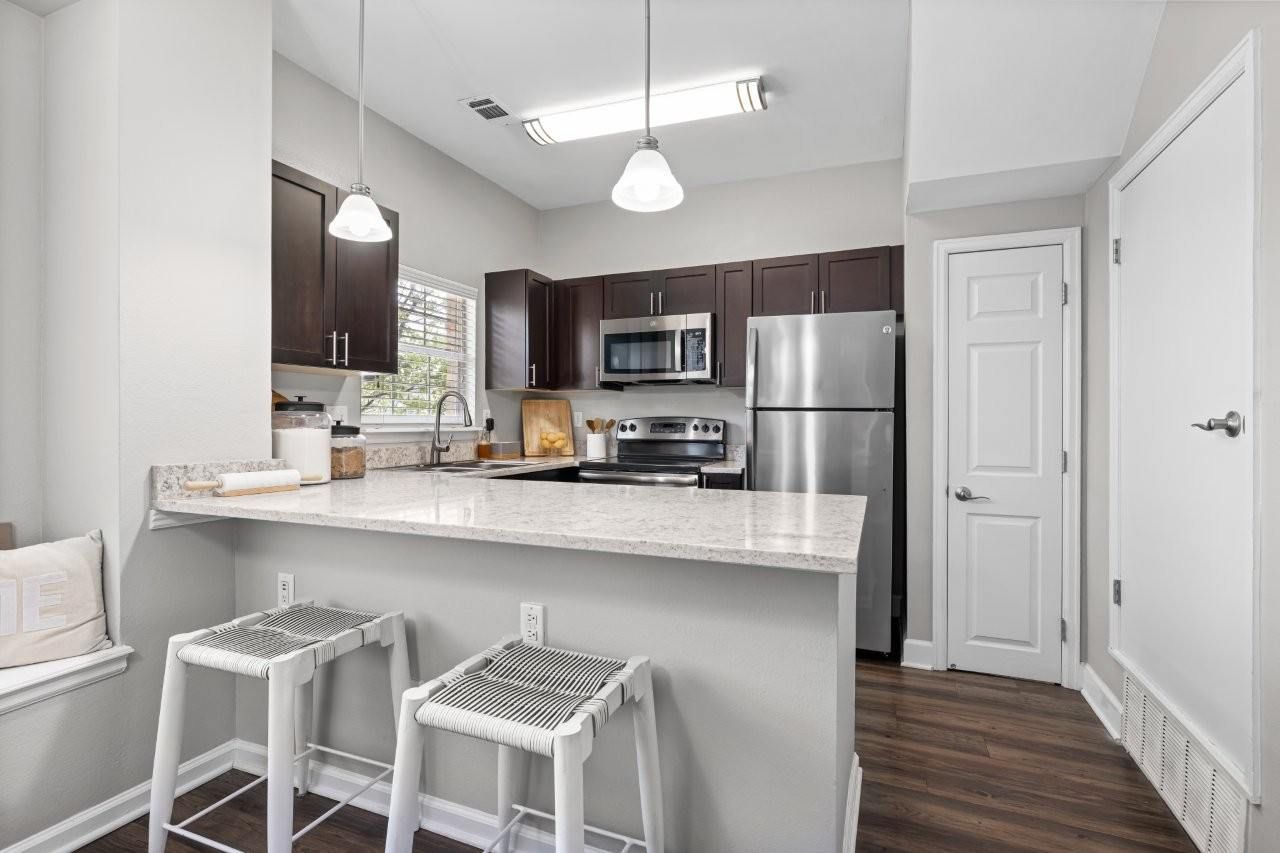 Modern apartment kitchen with granite island, dark wood cabinets, and stainless steel appliances.