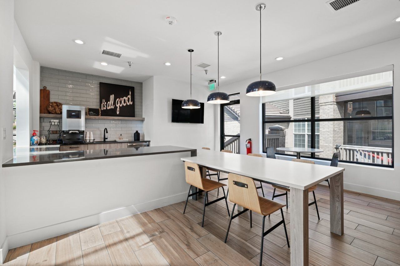 Modern communal kitchen and dining area with large window and pendant lights.
