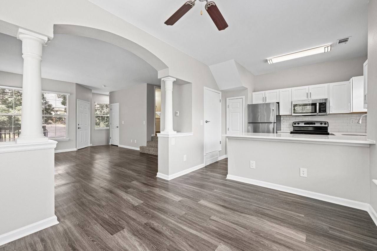 Open-concept living area with laminate flooring, white columns, and a kitchen with stainless steel appliances.