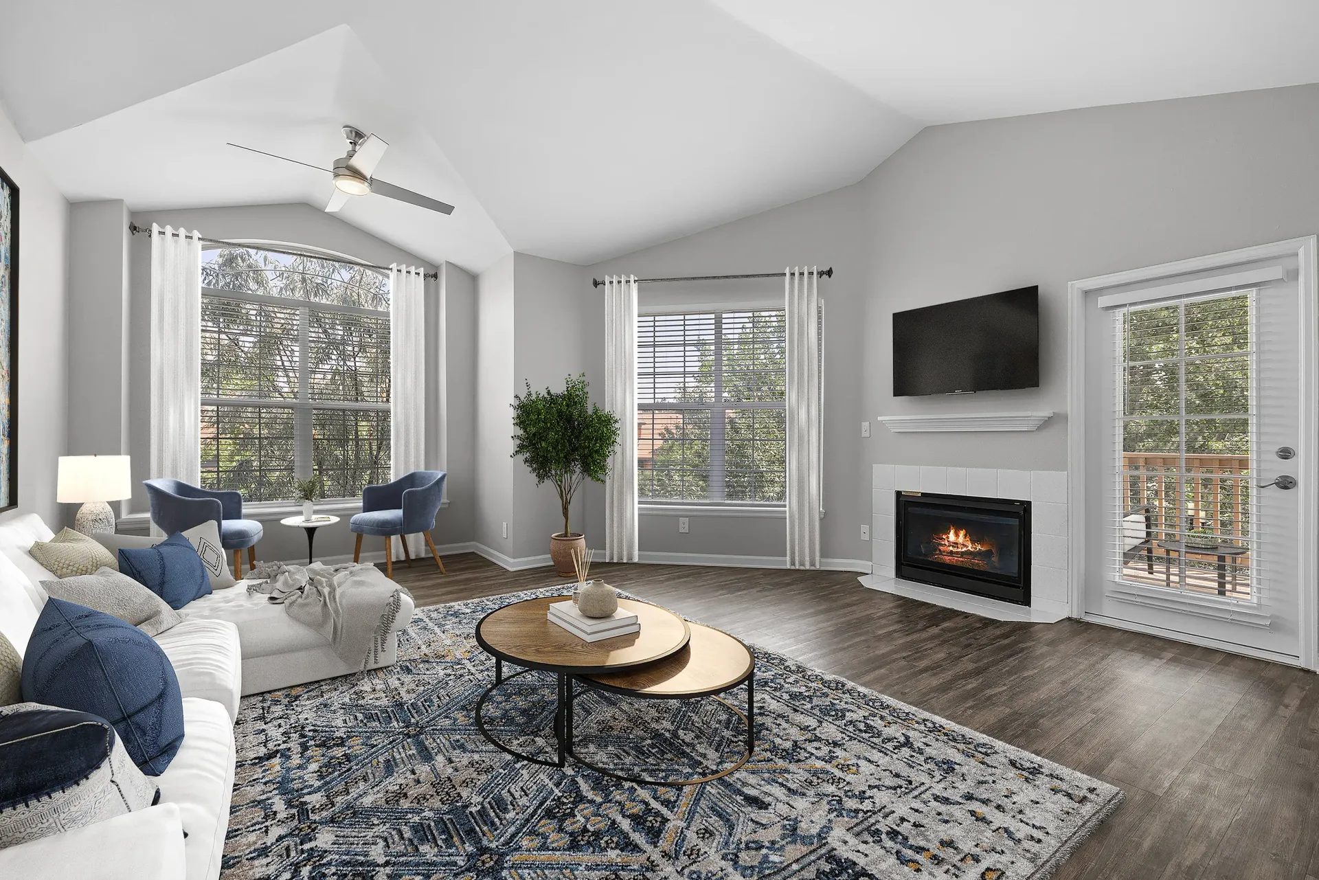 Spacious living room with large windows, white sofa, blue chairs, fireplace, and wall-mounted TV.
