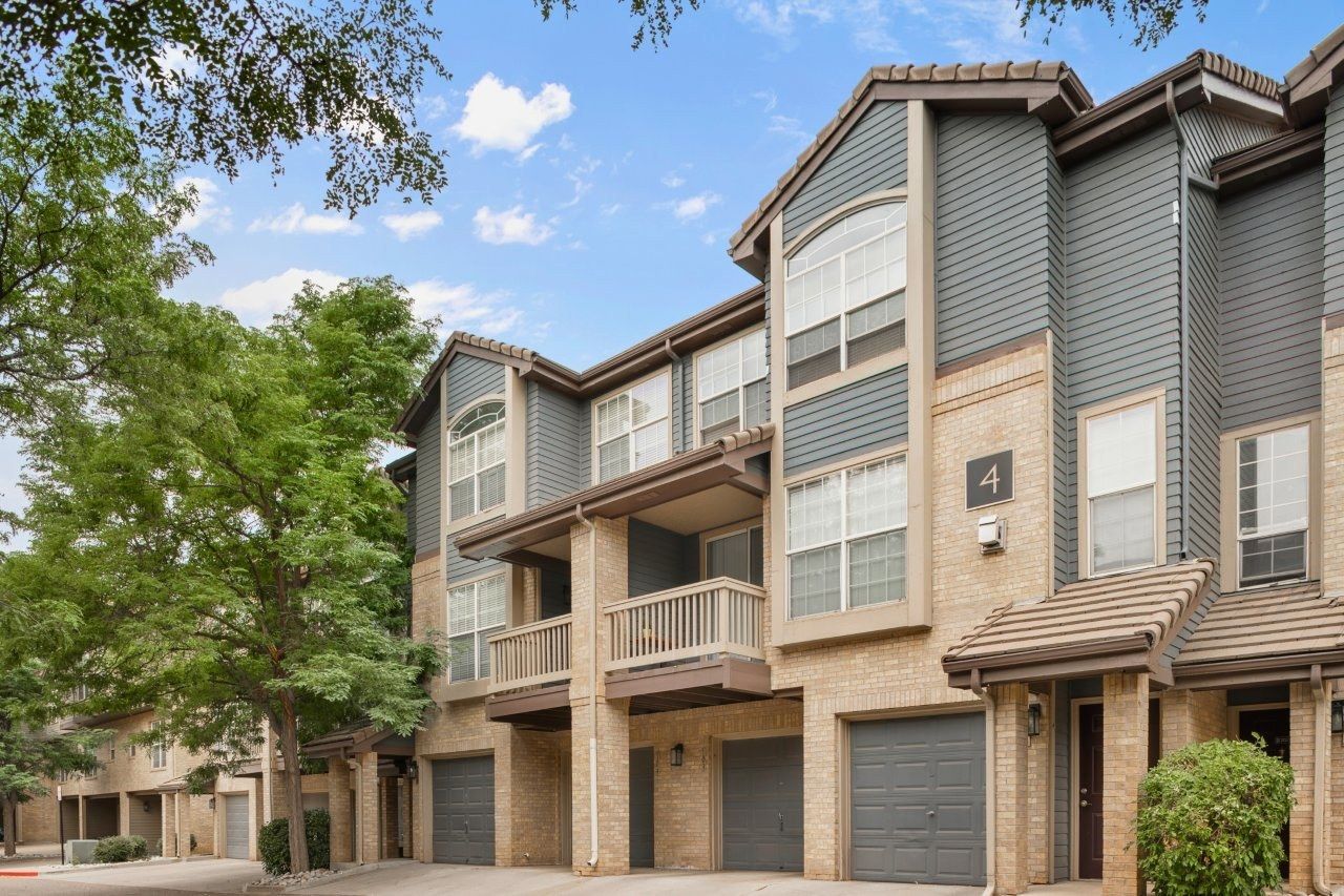 Exterior view of a modern apartment building with garages and trees.