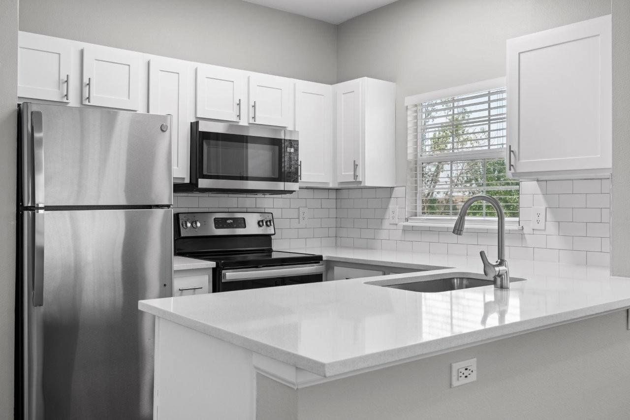 Bright modern apartment kitchen with white cabinets, stainless steel appliances, and a window over the sink.