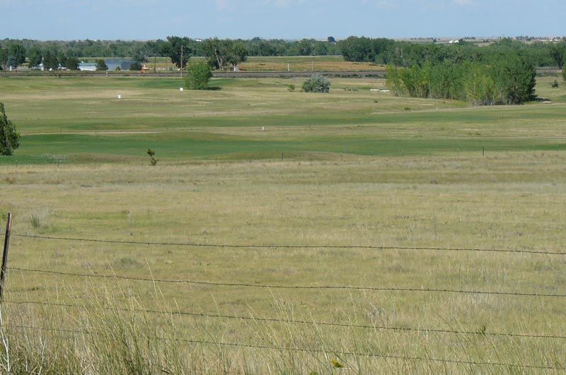 A large grassy field with a fence in the foreground