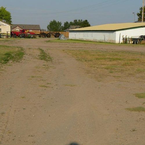 A dirt road with a white building in the background