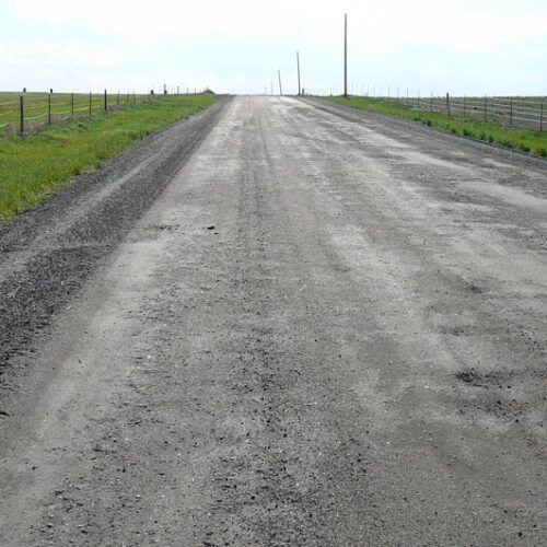 A dirt road going through a grassy field.